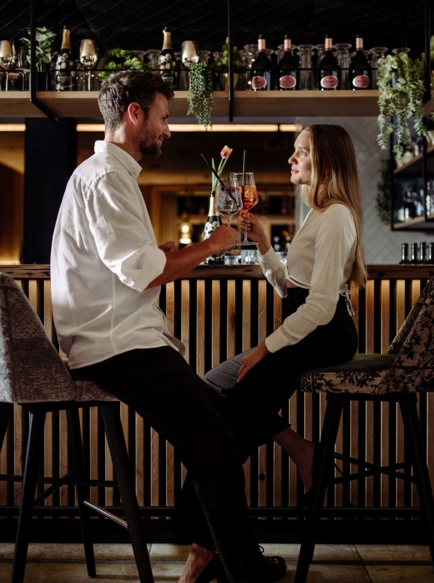 Paar sitzt an einer Bar und stößt mit Cocktails an